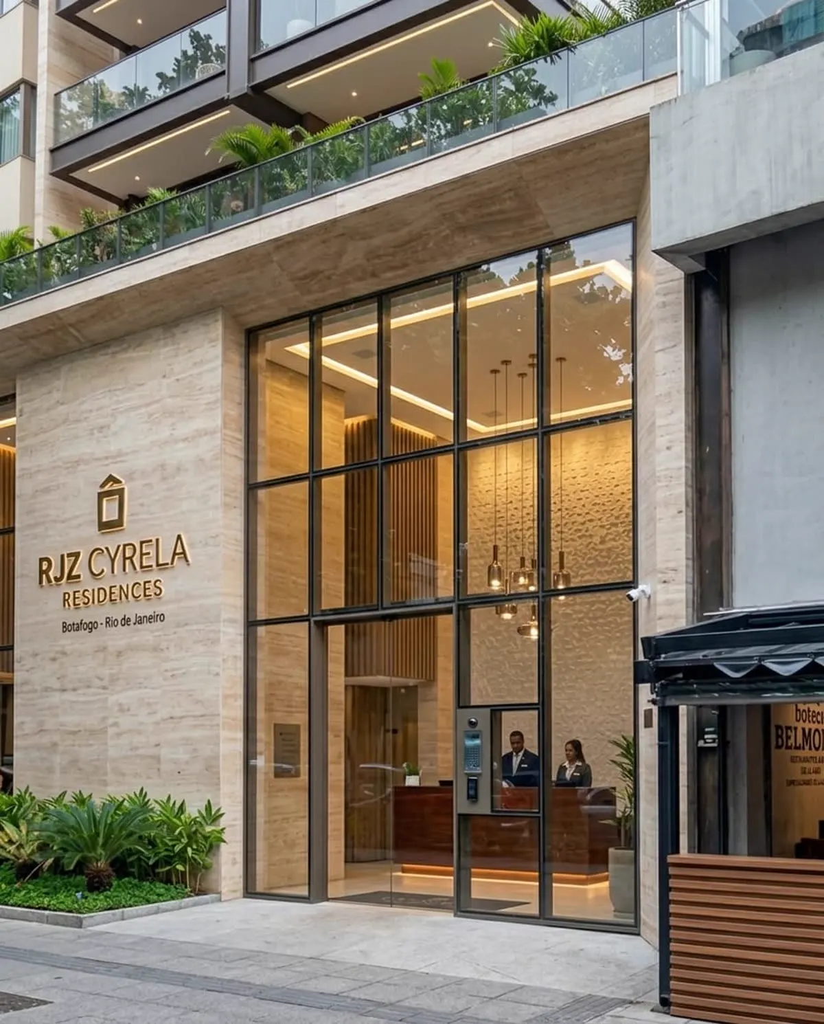 Entrada de edifício RJZ Cyrela Residences com revestimento em travertino e portaria iluminada